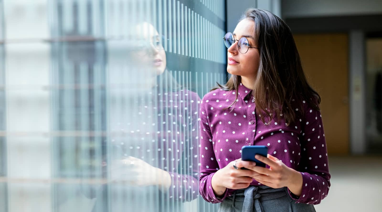 Woman holding a phone, in an office looking out of a window