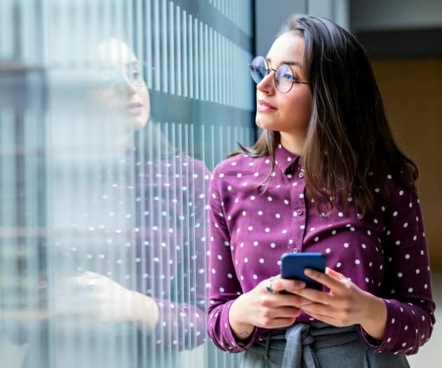 Woman holding a phone, in an office looking out of a window